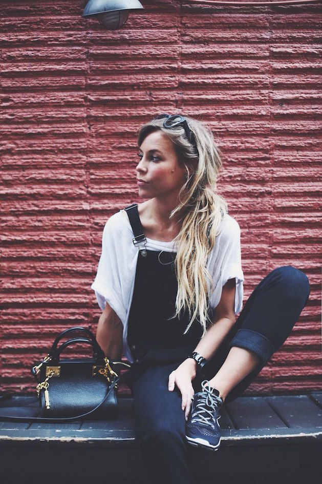 blonde woman in front of red wall with black overalls