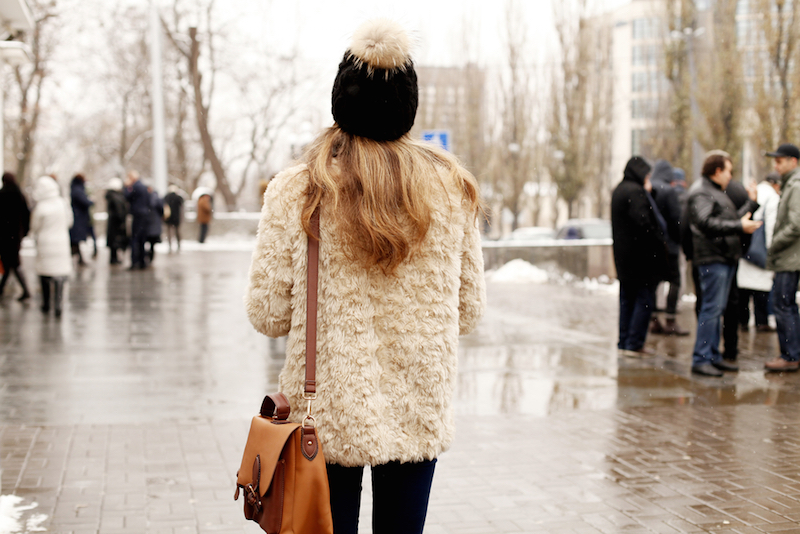 Outdoor close up portrait of fashionable woman posing on street. Model wearing stylish winter fake fur coat and beanie hat. Street style, fashion blogger outfit.