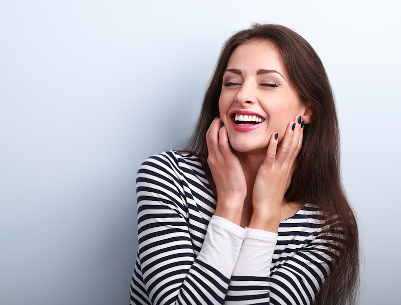 Happy loudly laughing woman holding hands the face on blue background
