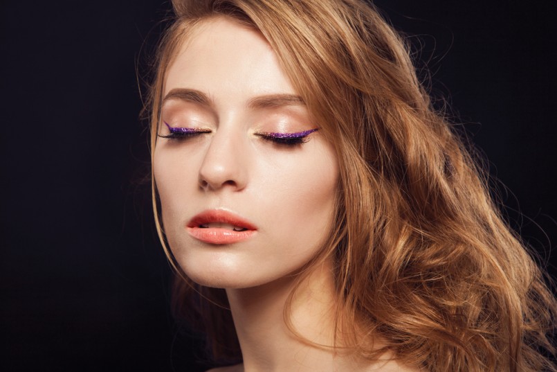 Beautiful woman with bright make up eye with sexy purple sparky gloss liner makeup. Fashion big arrow shape on woman's eyelid. Chic evening make-up, healthy face,curly hair