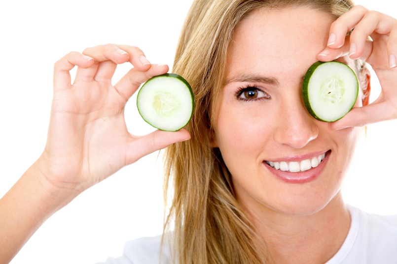 Woman with a slice of cucumber in her eye - isolated over a white background