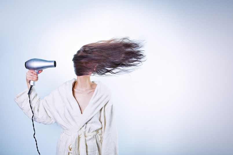 brunette woman blow drying her hair with blue background
