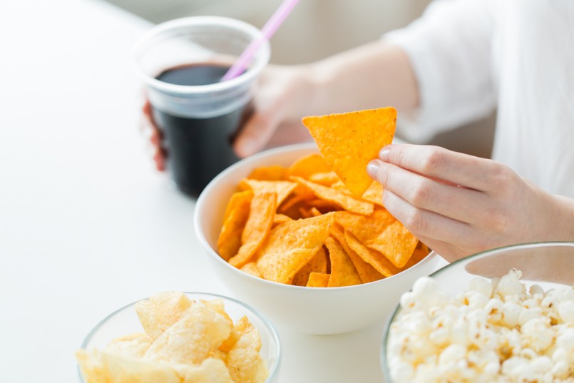 people, fast food, junk-food and unhealthy eating concept - close up of woman with popcorn, nachos or corn crisps and peanuts in bowls