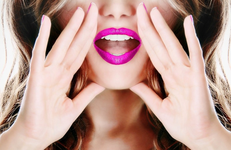 Attractive young sexy woman with pink lipstick lipgloss lips is announcing, telling a secret, shouting or yelling