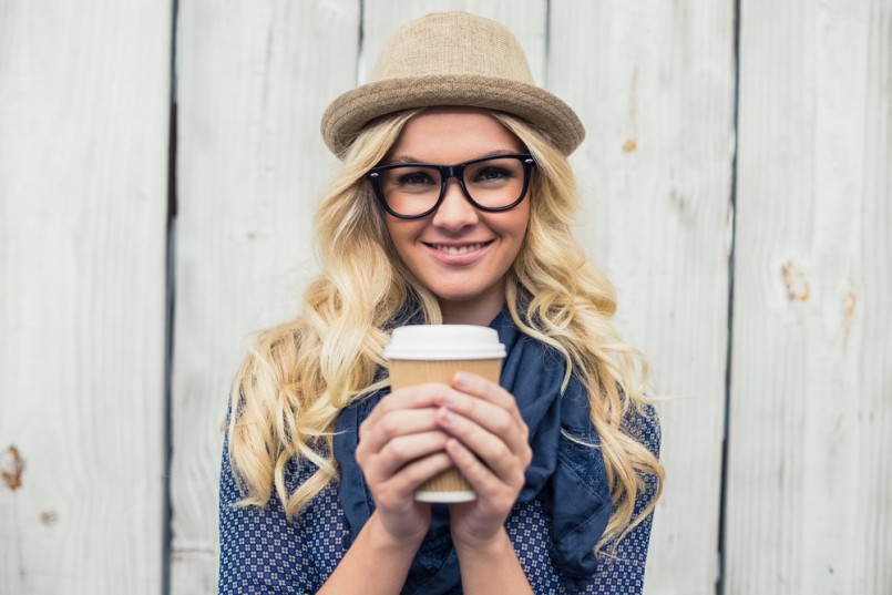 Cheerful fashionable blonde holding coffee outdoors on wooden background