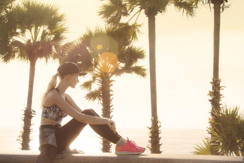 Beautiful young woman relaxing close to the sea after the hard workout and watching sunset. Golden colors made nice feeling and matching with long blonde hair of the girl
