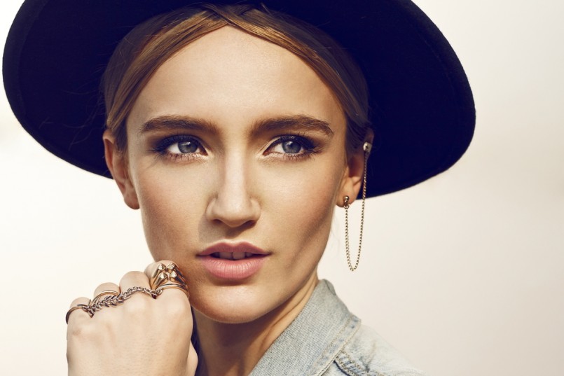 Close up of beautiful young blonde woman with black hat. Wearing denim vest. Her hair is tied to ponytail. Professional make-up, hair style and styling