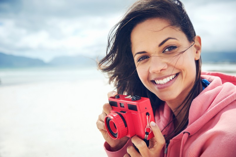 Portrait of beautiful Latino woman with retro hipster camera having fun at the beach