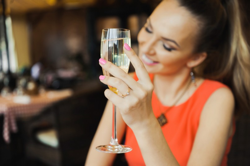 close-up portrait of a beautiful young elegant sexy blonde woman in the cafe with a glass of champagne,White wine smiling and drink posing, with a ring on her finger, she is engaged
