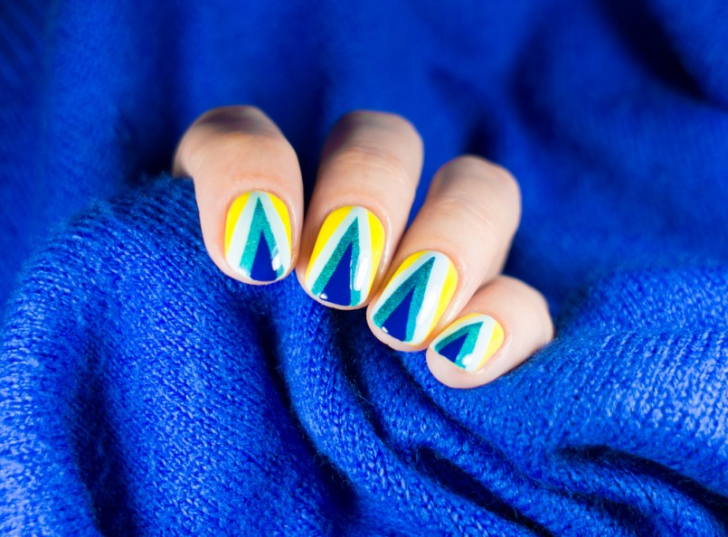 Beautiful manicure. Nail polish being applied to hand, polish is a blue color. Blue background closeup