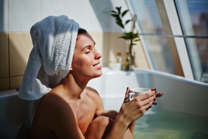 Relaxed girl sitting in bath with cup of herbal tea