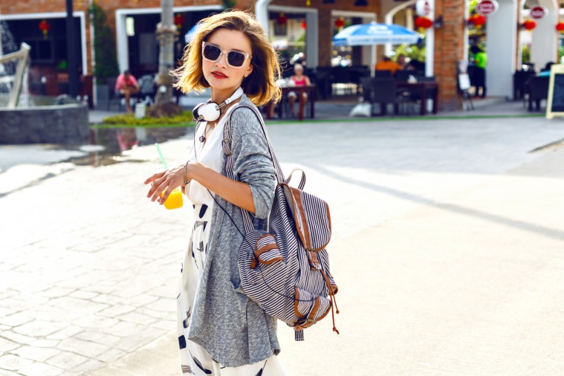 Summer sunny lifestyle fashion portrait of young stylish hipster woman walking on the street, wearing cute trendy outfit, drinking tasty smoothie, smiling enjoy her weekends, travel with backpack
