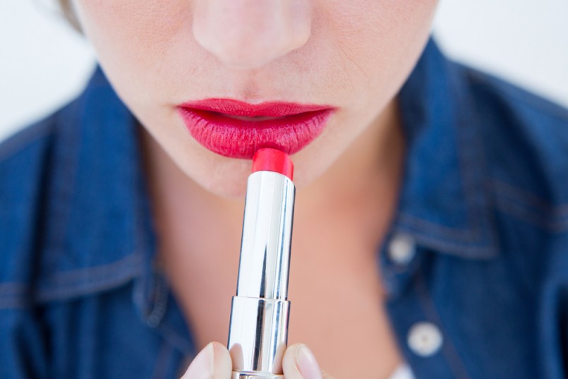Woman putting red lipstick on white background