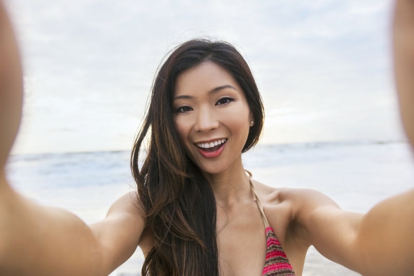 Asian young woman or girl in bikini, taking vacation selfie photograph at the beach