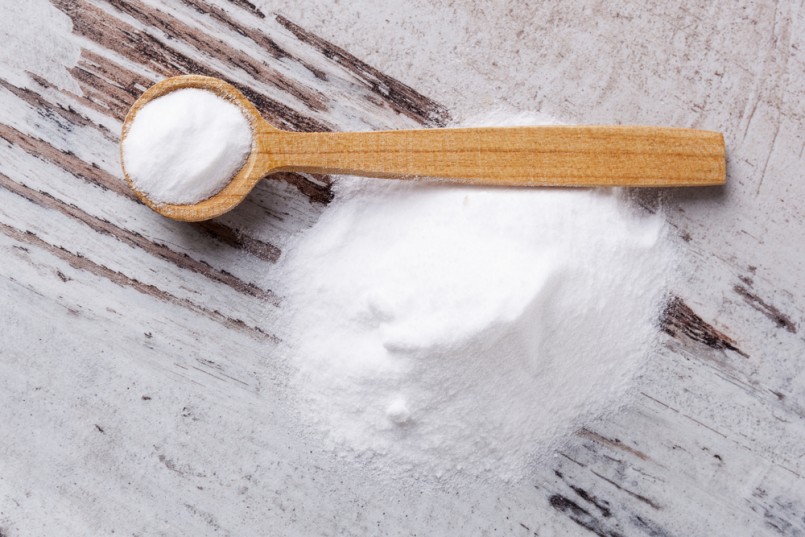 Baking soda on wooden spoon on white wooden textured background