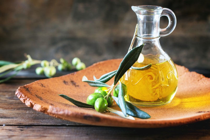 Battle of olive oil with olive branch in handmade clay plate over wooden table.