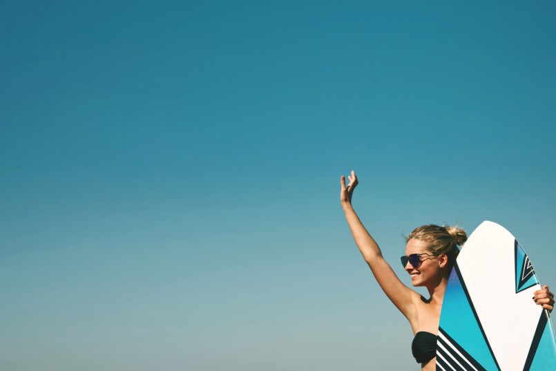 Blonde girl dressed in swimsuit standing on the ocean ready to surfing, female surfer holding surfboard