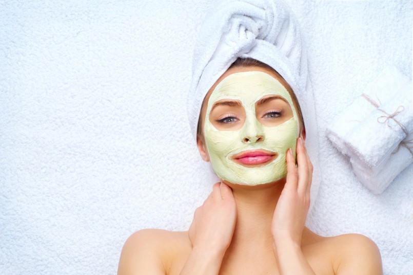 Spa Woman applying Facial clay Mask. Beauty Treatments. Close-up portrait of beautiful girl with a towel on her head applying facial mask