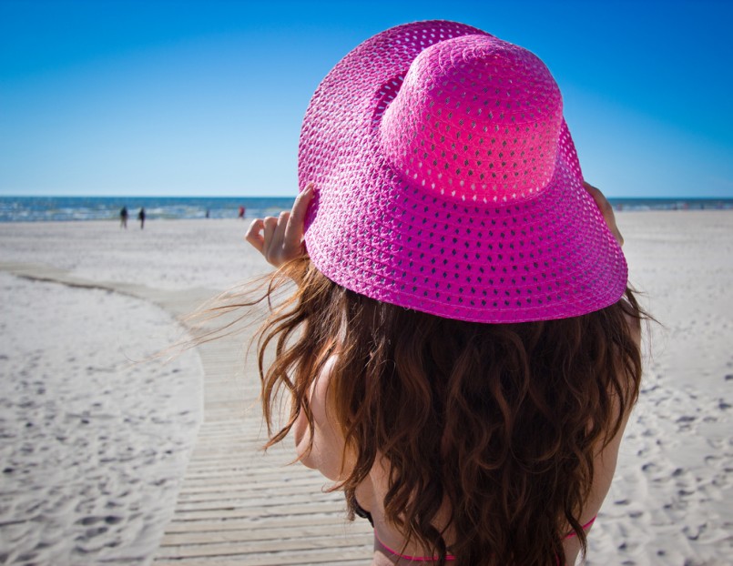 Young woman with long brown hair and big pink hat on the beach