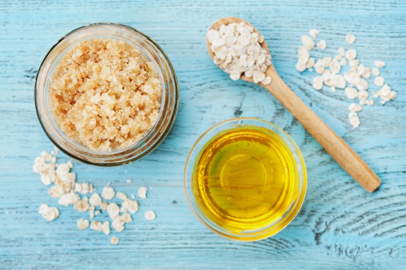 Body scrub of oatmeal, sugar, honey and oil in glass jar on blue rustic table, homemade cosmetic for peeling and spa care, top view