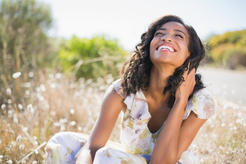 Happy pretty woman sitting on the grass in floral dress on a sunny day in the countryside