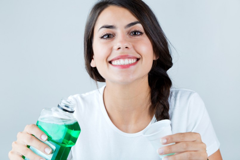 Portrait of beautiful girl using mouthwash. Isolated on white