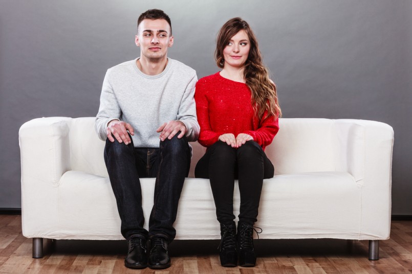 Shy woman and man sitting on sofa couch next each other. First date. Attractive girl and handsome guy meeting dating and trying to talk.