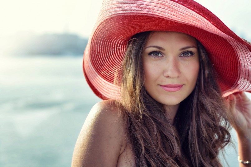 Beautiful girl in a red hat smiling at the summer waterfront