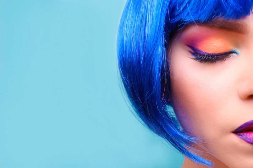 Beautiful girl with colorful makeup and wig on blue background