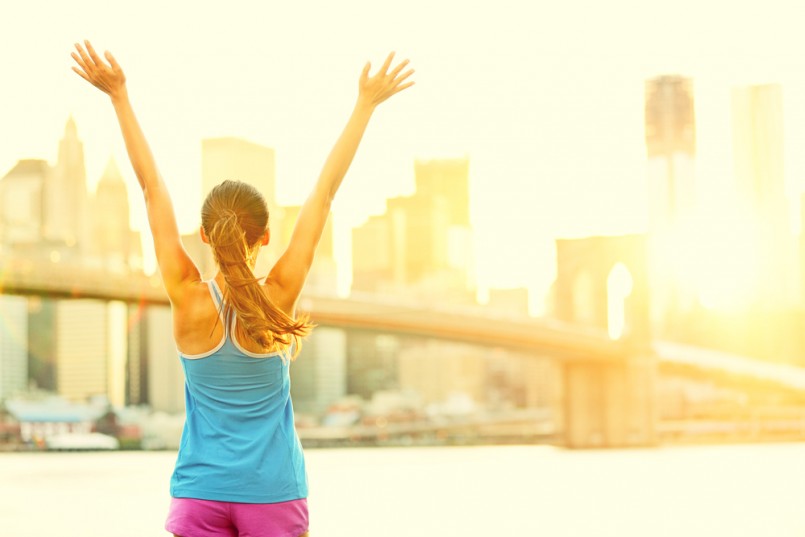 Happy cheering woman in New York City enjoying view and sun on Brooklyn Bridge. Fit female fitness runner joyful and excited after running