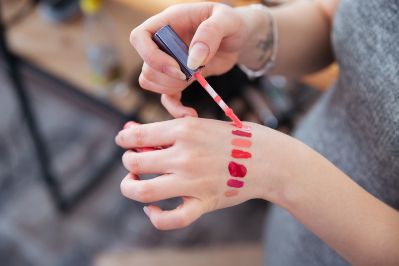Closeup of hands of woman makeup artist testing lip gloss different colors on her hand