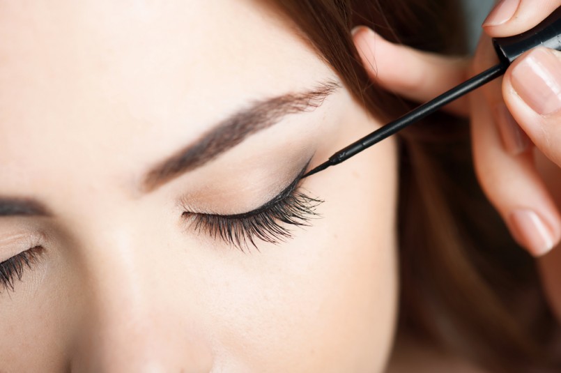 Close-up portrait of beautiful girl touching black eyeliner to her eyelid. Her eyes are closed