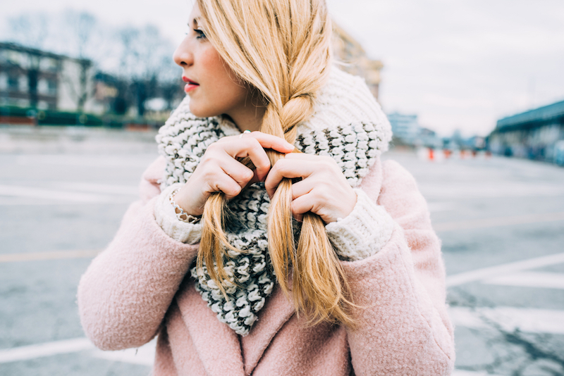 Close up on hands of young beautiful caucasian blonde woman weaving her hair on a braid - hair styling, care concept