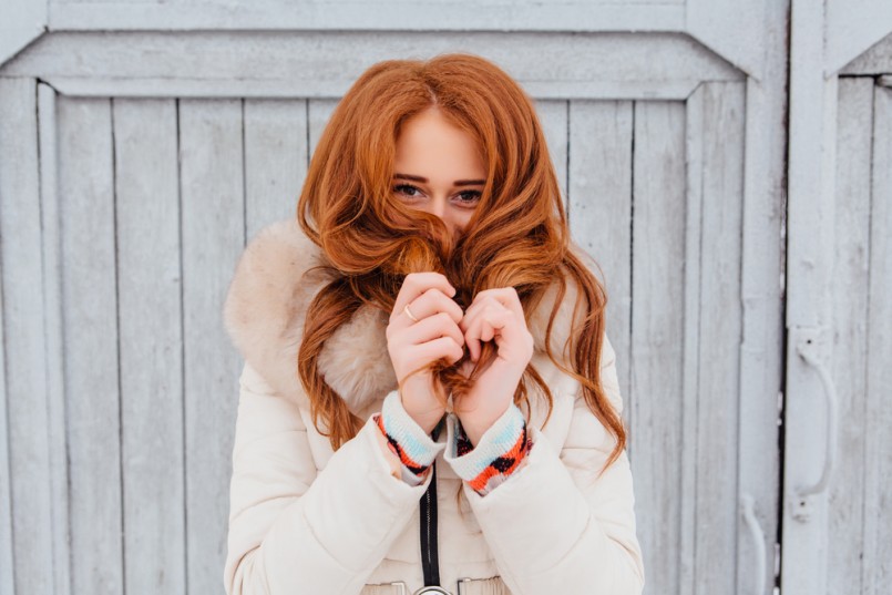 Portrait of a beautiful red hair young woman in warm clothes outdoor on the grey wooden background. Girl shows different emotions